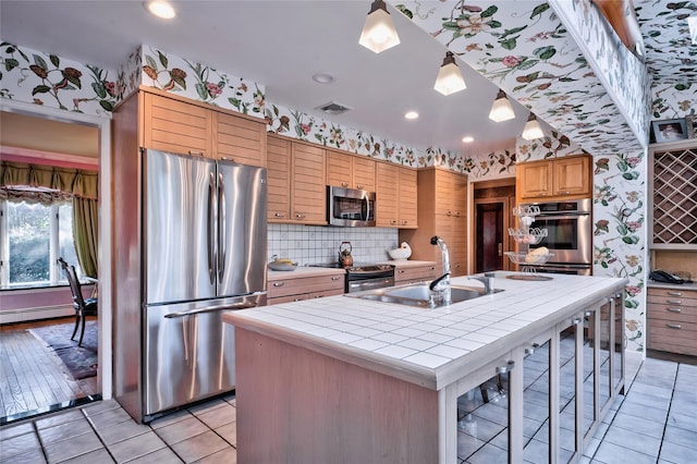 kitchen with tile countertops, sink, hanging light fixtures, a kitchen island with sink, and stainless steel appliances