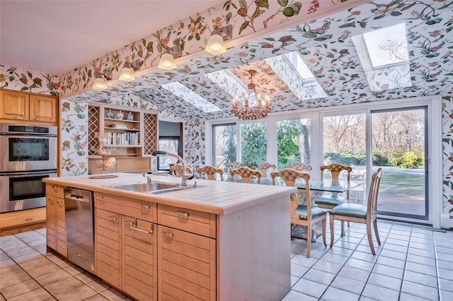 kitchen featuring tile countertops, a skylight, sink, stainless steel appliances, and a center island with sink