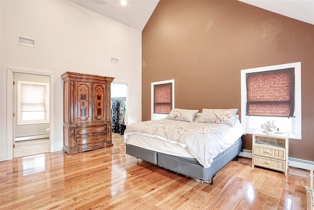 bedroom with high vaulted ceiling, baseboard heating, multiple windows, and a spacious closet