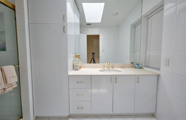 bathroom with tile patterned flooring, vanity, a skylight, and tile walls