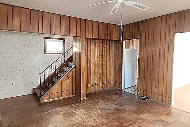 interior space featuring ceiling fan, wood walls, and parquet floors