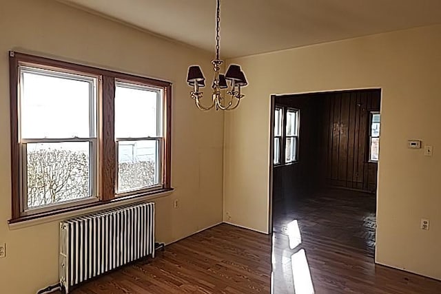 unfurnished dining area featuring radiator heating unit, dark hardwood / wood-style floors, and an inviting chandelier