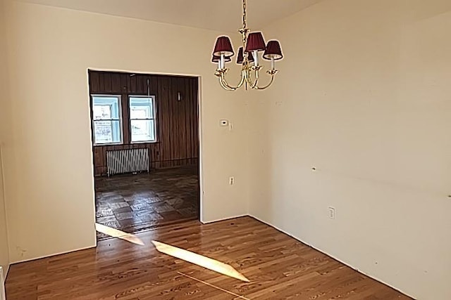 unfurnished dining area featuring radiator heating unit, dark wood-type flooring, and a notable chandelier