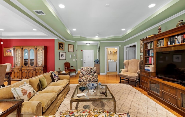 living room featuring hardwood / wood-style flooring, crown molding, washer / dryer, and a raised ceiling