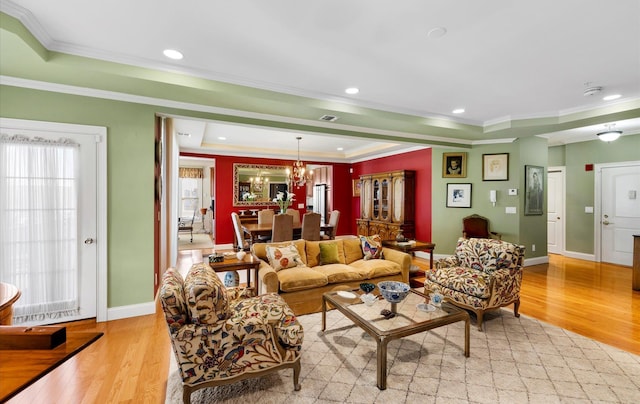 living room featuring a tray ceiling, ornamental molding, a chandelier, and light wood-type flooring