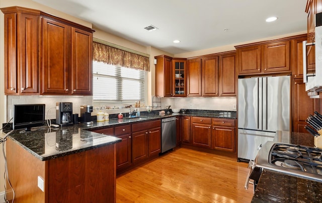 kitchen featuring appliances with stainless steel finishes, dark stone counters, sink, backsplash, and light wood-type flooring