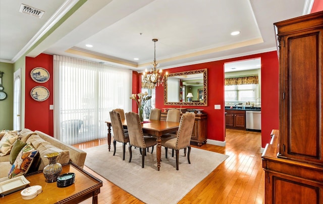 dining room with crown molding, a tray ceiling, a chandelier, and light hardwood / wood-style floors