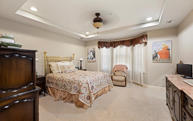 bedroom with ceiling fan, light colored carpet, and a raised ceiling