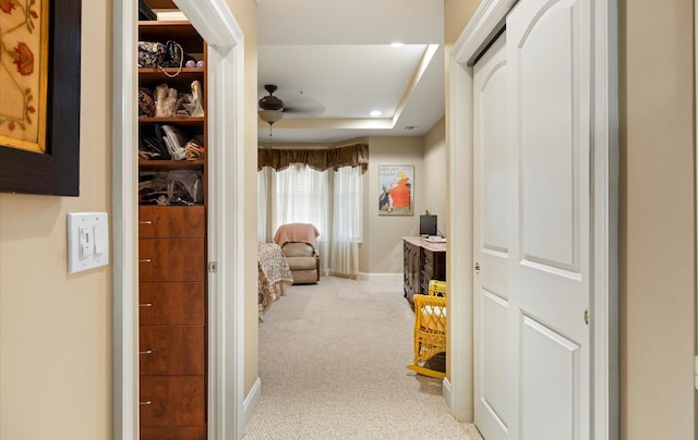 corridor featuring a raised ceiling and light carpet