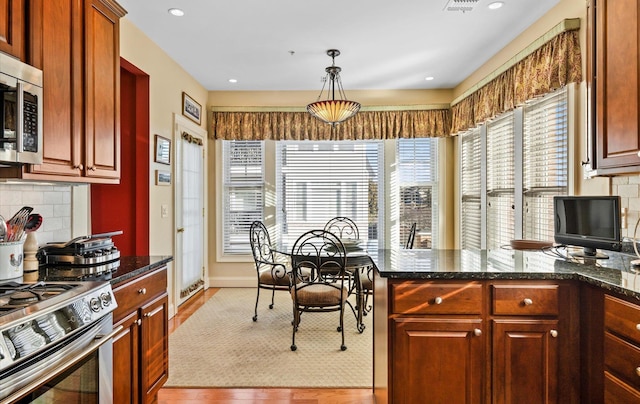 kitchen featuring appliances with stainless steel finishes, decorative light fixtures, dark stone countertops, tasteful backsplash, and light hardwood / wood-style flooring