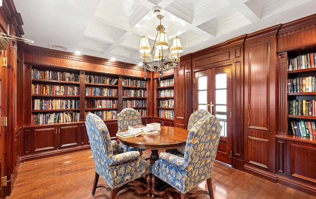 dining area featuring wood walls, beamed ceiling, an inviting chandelier, coffered ceiling, and built in shelves