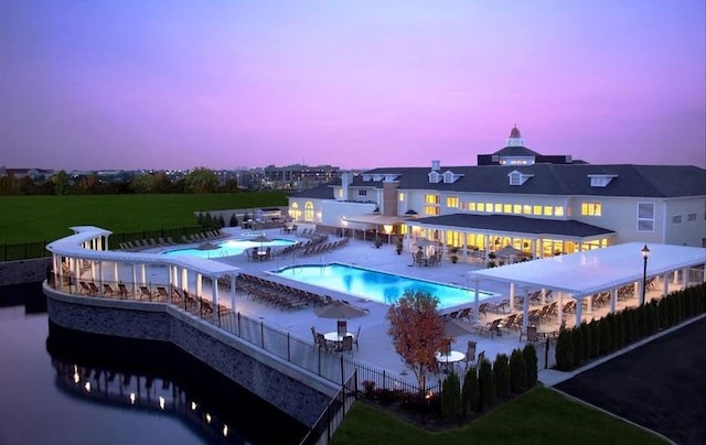 pool at dusk with a patio area, a lawn, and a water view