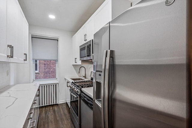 kitchen featuring appliances with stainless steel finishes, light stone counters, sink, radiator heating unit, and white cabinetry