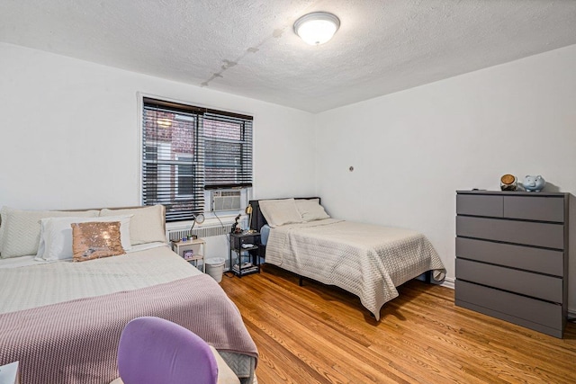 bedroom featuring cooling unit, a textured ceiling, and light hardwood / wood-style flooring