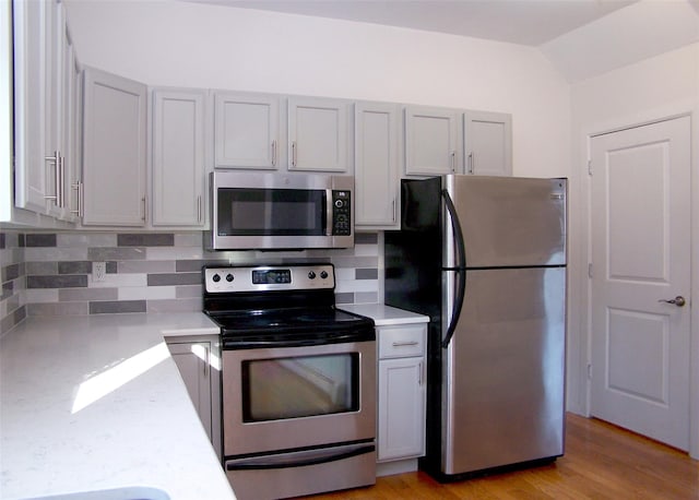 kitchen with lofted ceiling, stainless steel appliances, light wood-type flooring, and tasteful backsplash