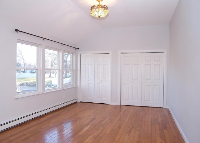 unfurnished bedroom with lofted ceiling, a baseboard heating unit, hardwood / wood-style flooring, and multiple closets