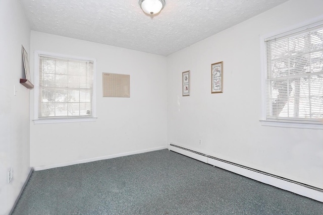 empty room featuring a textured ceiling, a baseboard heating unit, a healthy amount of sunlight, and dark colored carpet