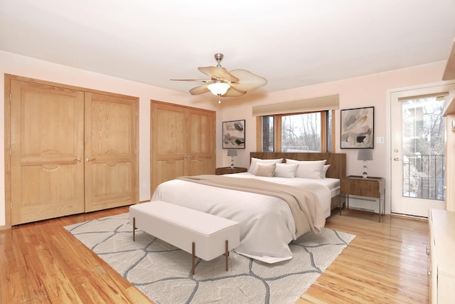 bedroom featuring baseboard heating, ceiling fan, two closets, light hardwood / wood-style flooring, and access to outside