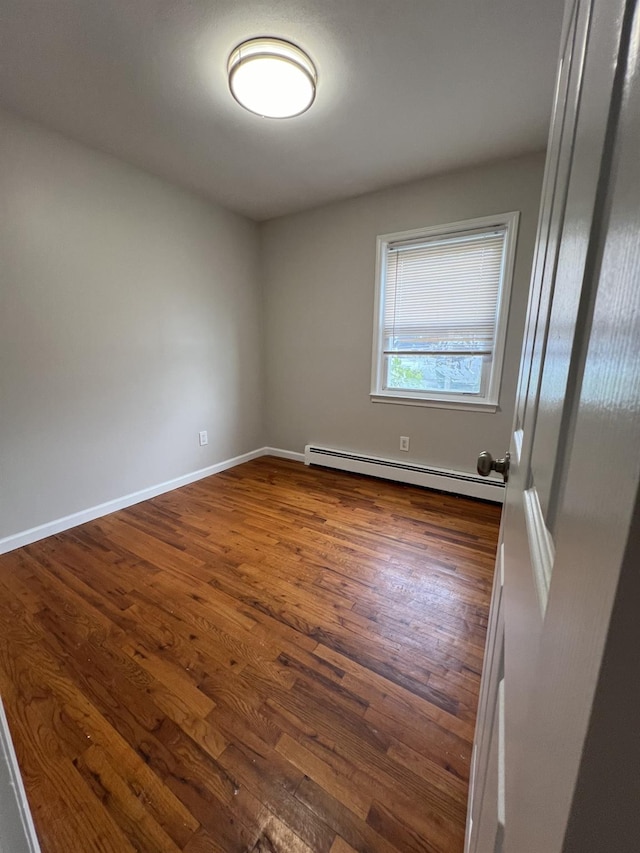 spare room with dark hardwood / wood-style flooring and a baseboard heating unit