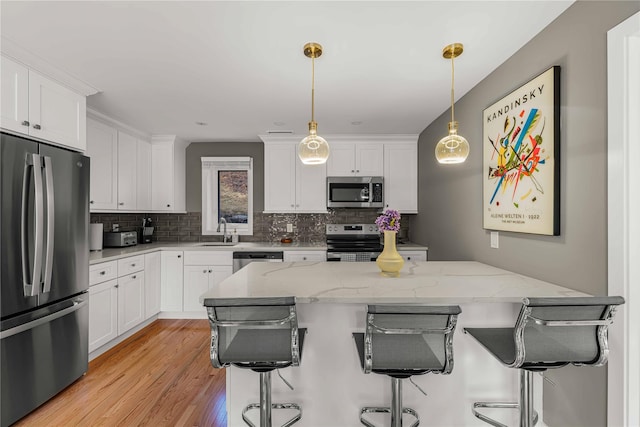 kitchen with white cabinets, light stone countertops, stainless steel appliances, and hanging light fixtures