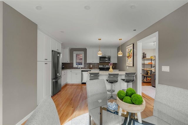 kitchen featuring decorative backsplash, appliances with stainless steel finishes, light wood-type flooring, white cabinets, and hanging light fixtures