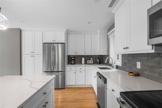 kitchen with sink, hanging light fixtures, light stone countertops, white cabinetry, and stainless steel appliances