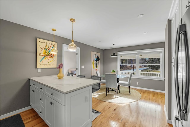 kitchen with light stone counters, light hardwood / wood-style flooring, pendant lighting, black refrigerator, and white cabinets