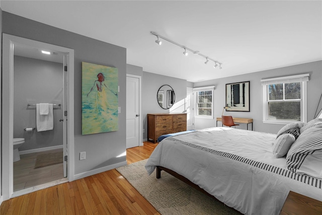 bedroom with rail lighting, light wood-type flooring, multiple windows, and ensuite bath