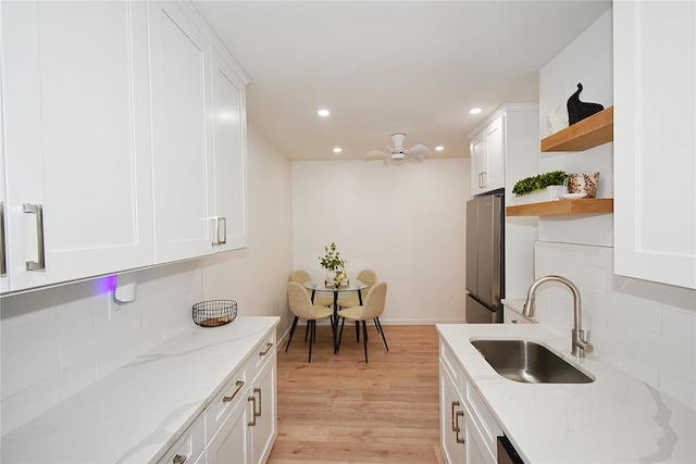 kitchen featuring sink, stainless steel fridge, white cabinets, light stone countertops, and light hardwood / wood-style flooring