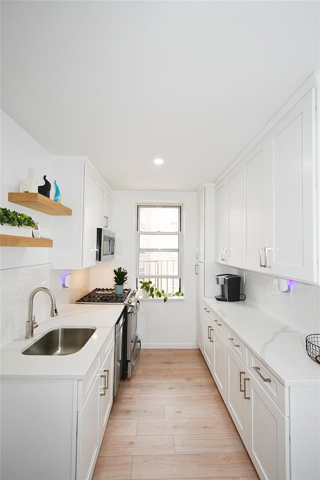 kitchen with stainless steel appliances, sink, white cabinets, and light hardwood / wood-style flooring