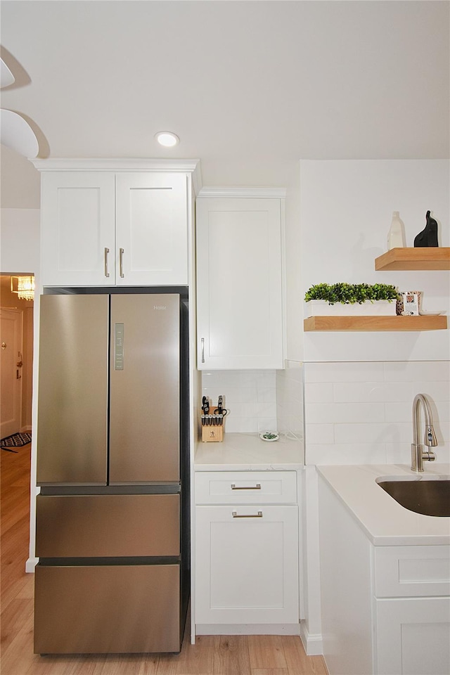 kitchen with sink, light hardwood / wood-style flooring, fridge, decorative backsplash, and white cabinets