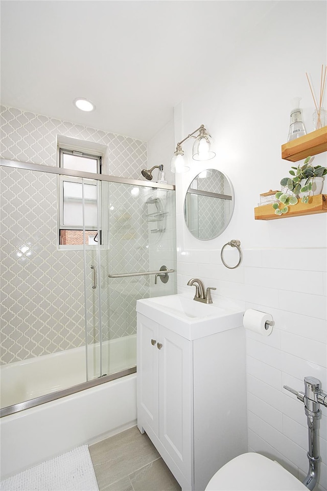 full bathroom with bath / shower combo with glass door, tile walls, vanity, and toilet