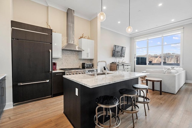 kitchen featuring wall chimney range hood, a breakfast bar, sink, hanging light fixtures, and paneled built in fridge