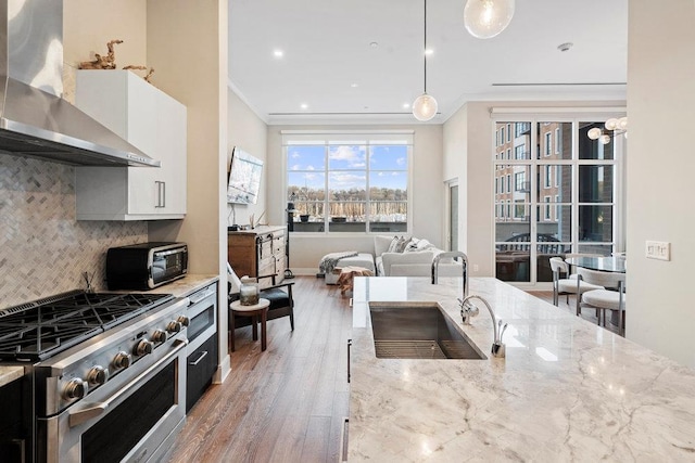 kitchen with white cabinetry, gas stove, decorative light fixtures, light stone countertops, and wall chimney range hood