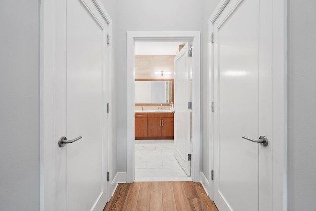 corridor with light wood-type flooring and sink