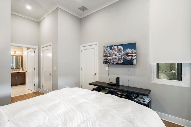 bedroom featuring a towering ceiling, ornamental molding, connected bathroom, and light hardwood / wood-style floors