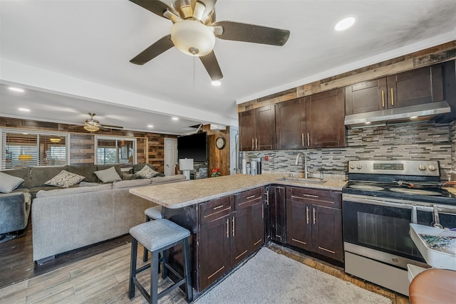 kitchen with a breakfast bar, kitchen peninsula, sink, light stone countertops, and stainless steel electric stove