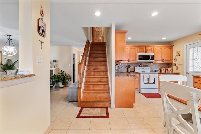 kitchen featuring tasteful backsplash, sink, white electric stove, hanging light fixtures, and light tile patterned flooring