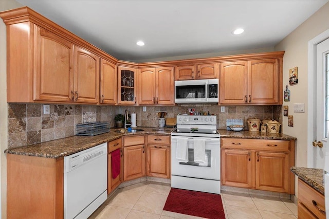 kitchen featuring decorative backsplash, dark stone counters, white appliances, sink, and light tile patterned floors