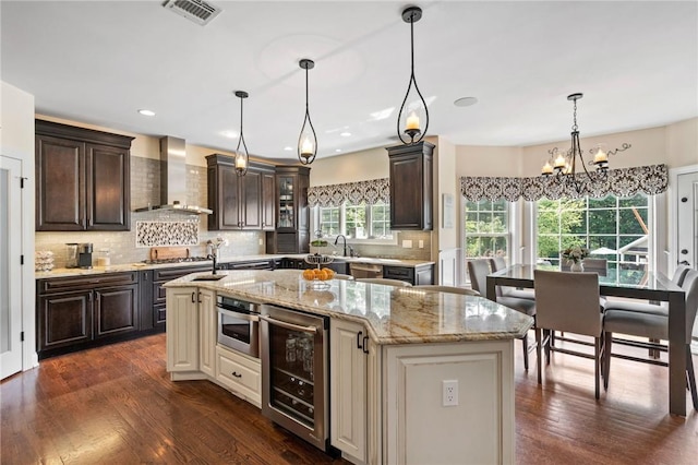 kitchen featuring wall chimney exhaust hood, beverage cooler, a chandelier, and a center island