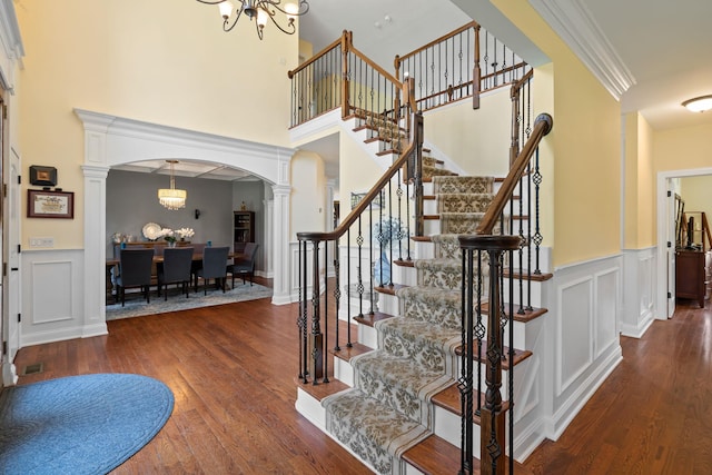 foyer entrance featuring ornate columns, dark hardwood / wood-style flooring, crown molding, and a notable chandelier