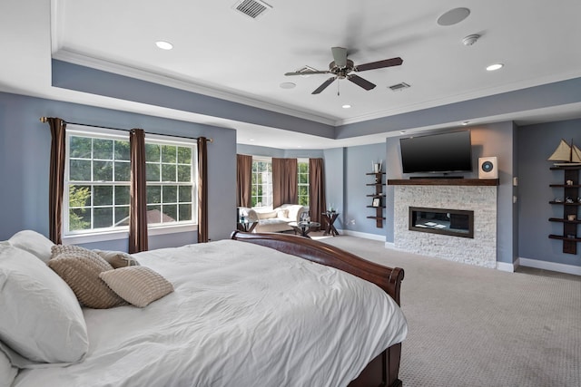 bedroom with a stone fireplace, crown molding, light carpet, ceiling fan, and a tray ceiling