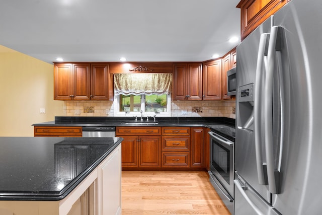 kitchen featuring stainless steel appliances, dark stone counters, sink, light hardwood / wood-style flooring, and tasteful backsplash