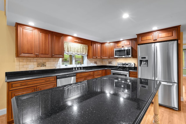 kitchen with sink, a center island, light hardwood / wood-style flooring, dark stone counters, and appliances with stainless steel finishes