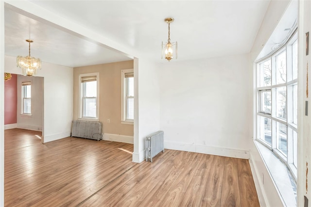 spare room with radiator, light hardwood / wood-style flooring, and an inviting chandelier