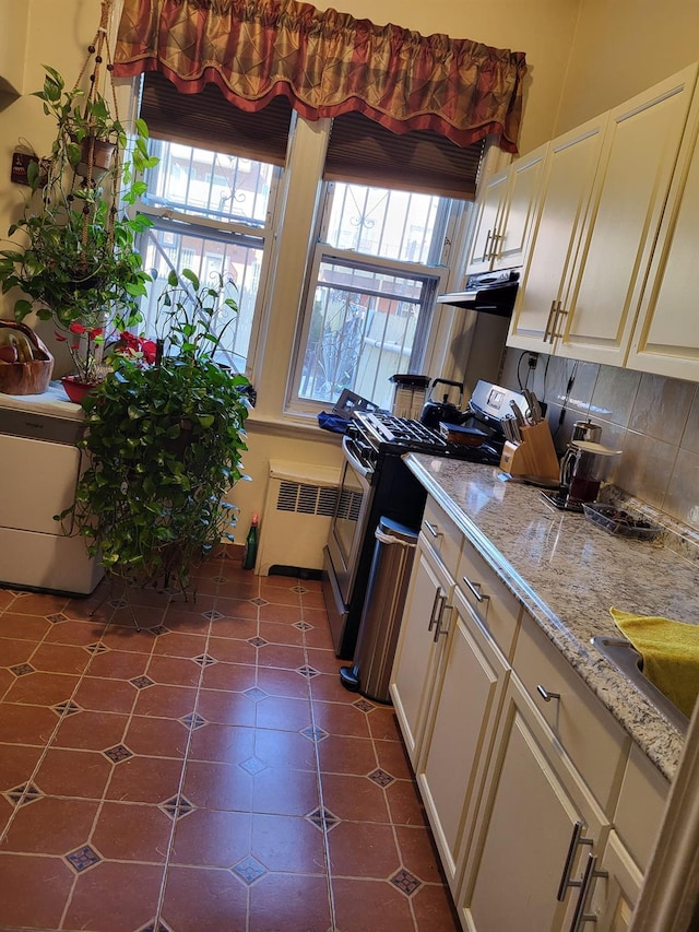 kitchen with light stone countertops, tasteful backsplash, dark tile patterned flooring, radiator heating unit, and stainless steel gas stove