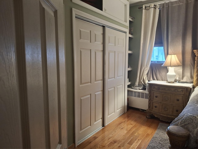 bedroom featuring light wood-type flooring, radiator heating unit, and a closet