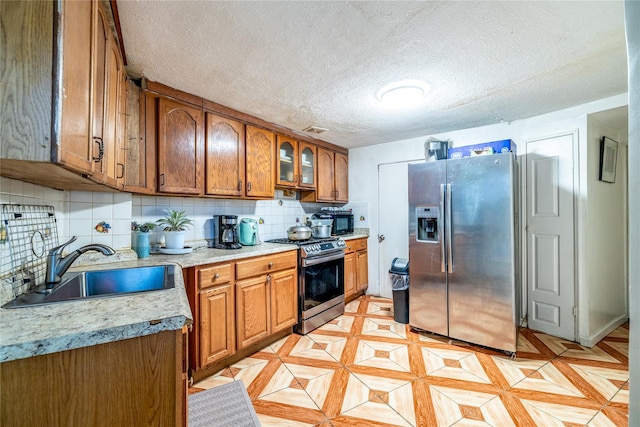 kitchen with a textured ceiling, backsplash, sink, and appliances with stainless steel finishes