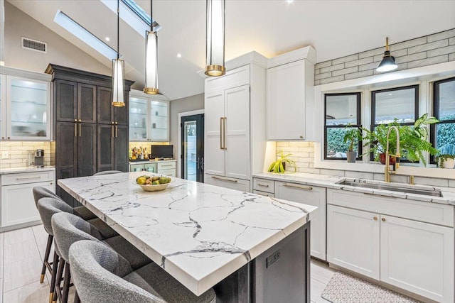 kitchen featuring a kitchen island, decorative light fixtures, tasteful backsplash, sink, and lofted ceiling with skylight