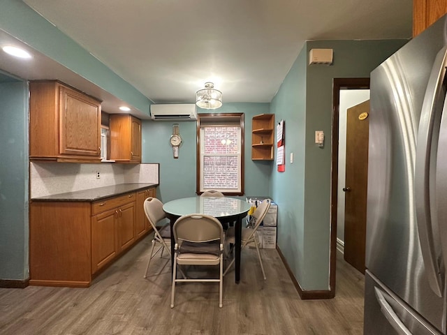 kitchen with a wall mounted air conditioner, hardwood / wood-style floors, backsplash, and stainless steel refrigerator